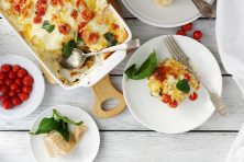 A casserole dish filled with freshly baked lasagna topped with tomatoes.