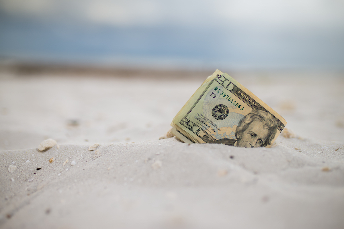 A stack of $20 bills is laid in the sand at a beach.