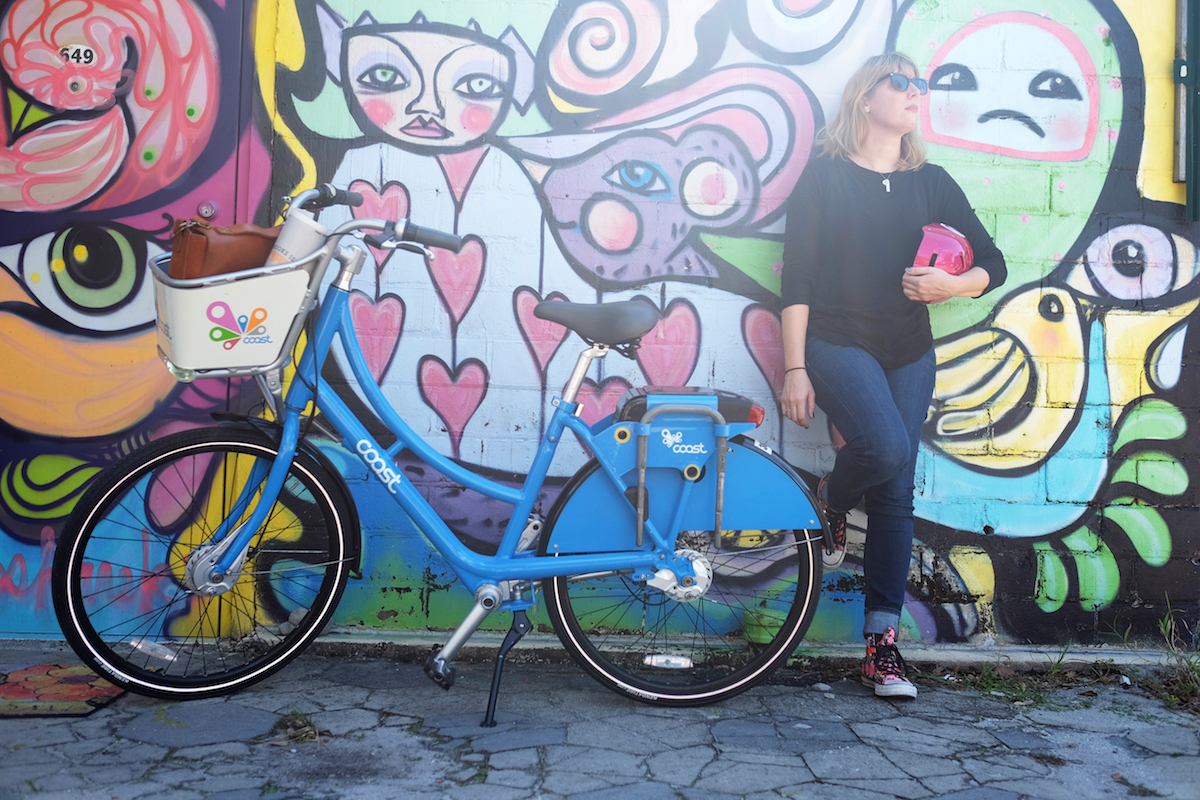 Lisa Rowan leaning against a wall next to a bicycle
