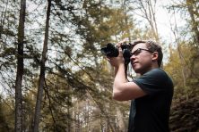 young man with nikon camera taking pictures in the woods