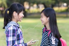 Two girls share earbuds to listen to music on their smartphone.