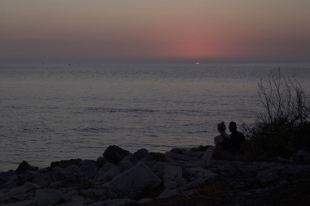 Two people watch as the sun sets on a beach in St. Petersburg, Fla.