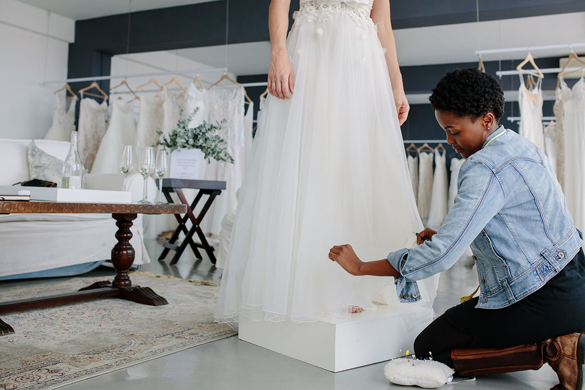 female bridal store employee making adjustment to bridal gown