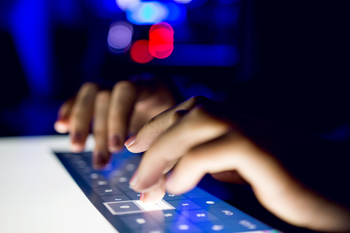 Hands Writing On Touch Screen Device Keyboard With Shallow Focus And Blurry Lights Behind