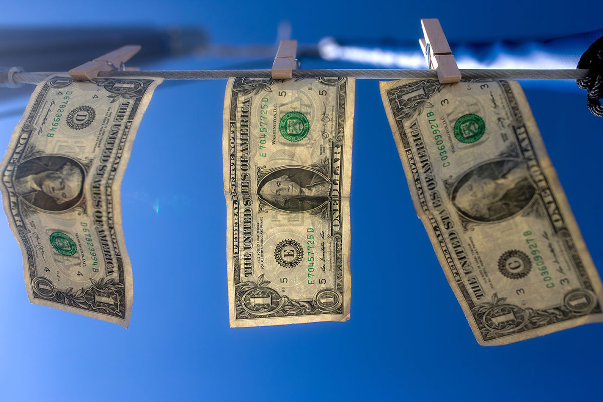 Dollar bills hang from a clothes line outside in the sunshine.