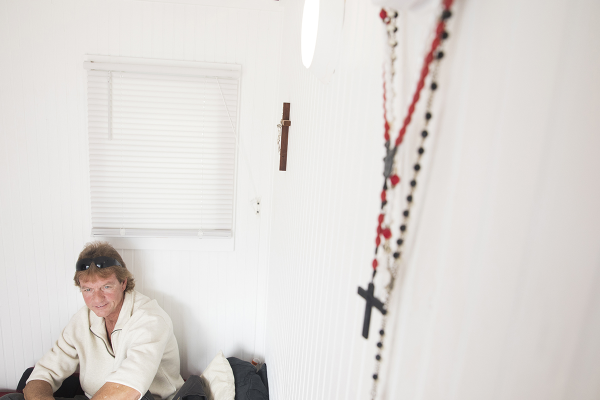 A homeless man sits on his bed in a homeless shelter.