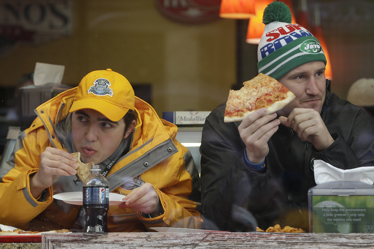 Super Bowl XLVIII volunteer Andrew Esoldi, left, of Englewood Clifs, N.J., and Peter Clark, a tourist from Australia, eat pizza on Super Bowl Boulevard on Jan. 29, 2014, in New York
