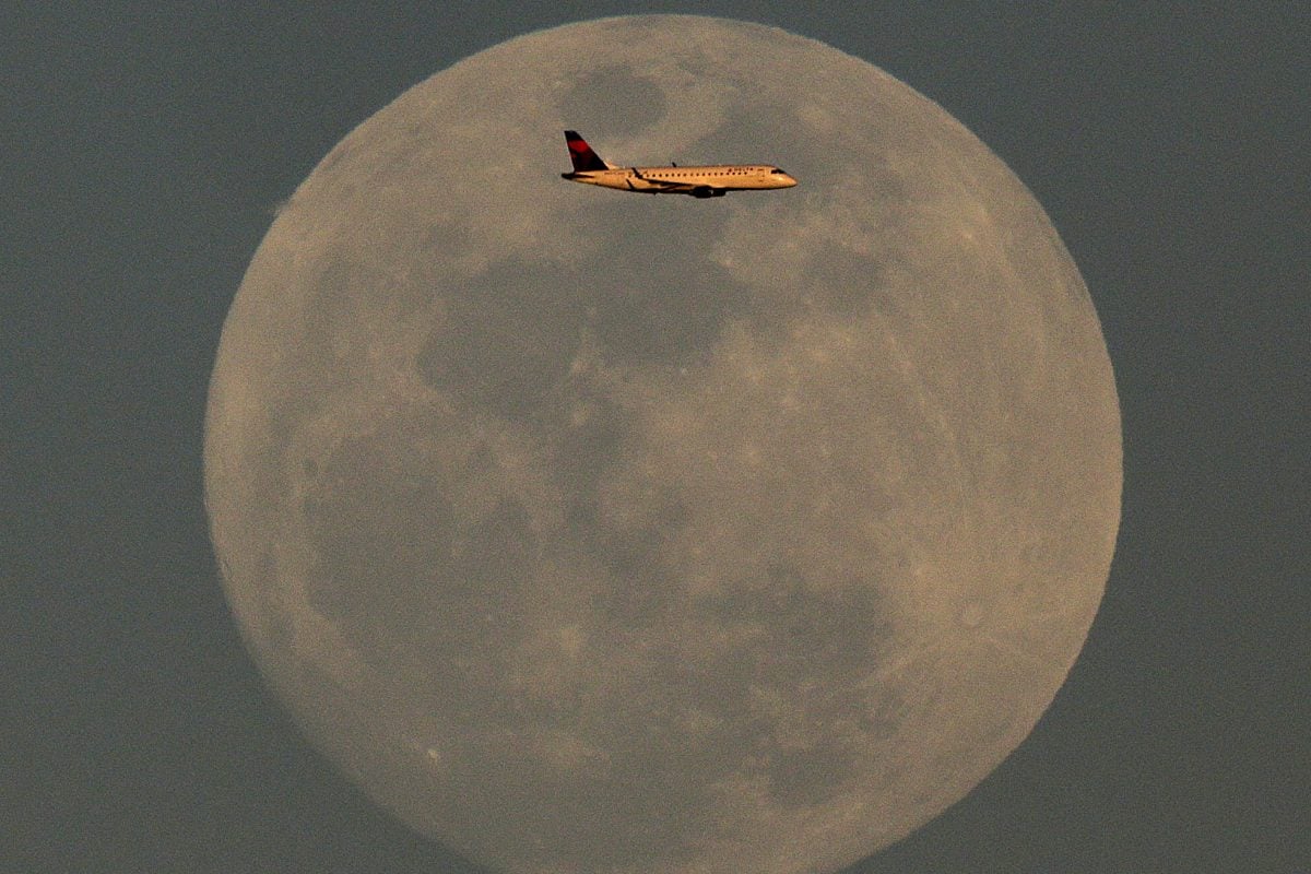 A Delta Airlines jet on approach to Sky Harbor International Airport passes the nearly full moon at it rises in the distance Sunday, Feb. 21, 2016, in Phoenix.
