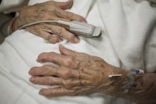 An senior citizen's hands rest on their midsection as they wear a hospital gown.
