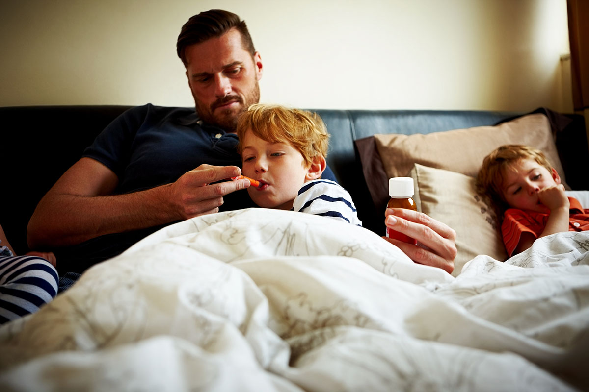 Father measuring temperature of his sick son, while lying on bed