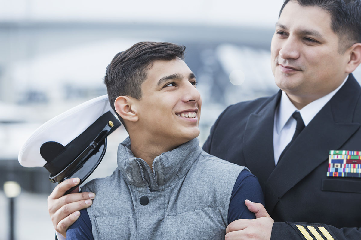 An Hispanic man wearing a military uniform, standing with his teenage son.