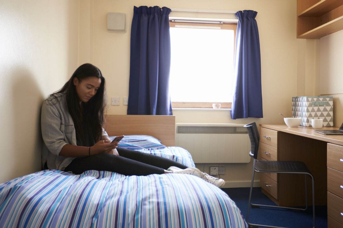 student using cell phone in college dorm room