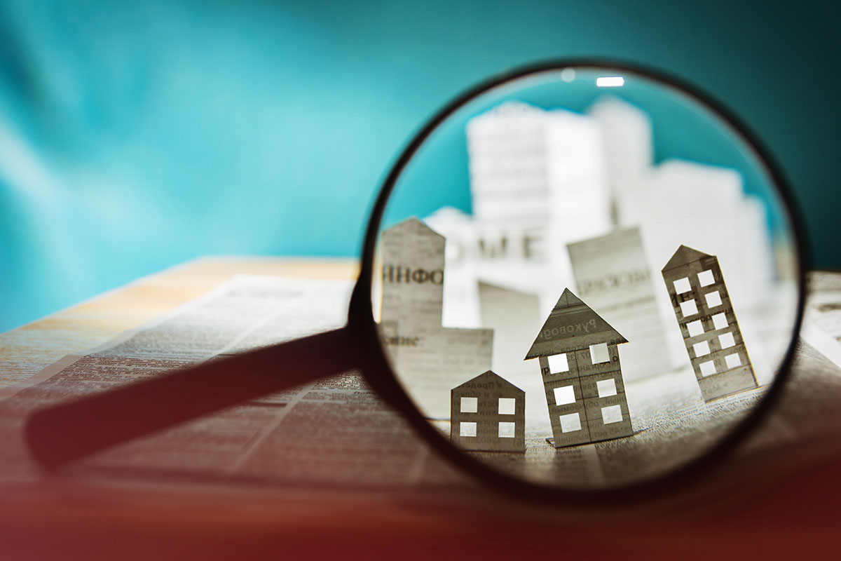 Magnifying glass in front of an open newspaper with paper houses.