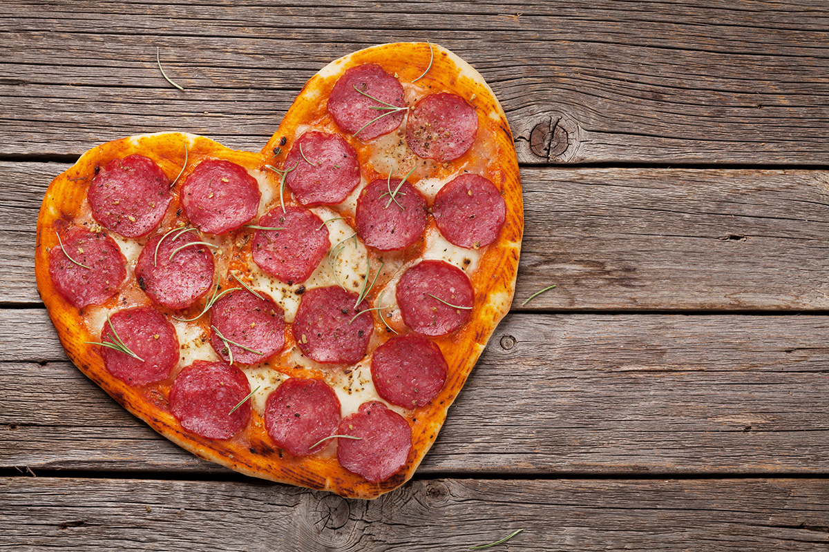 A freshly made pizza cut in a heart shape.