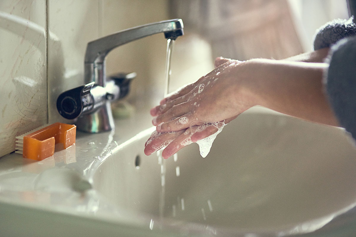 Shot of an unidentifiable young woman washing her hands by the bathroom sink