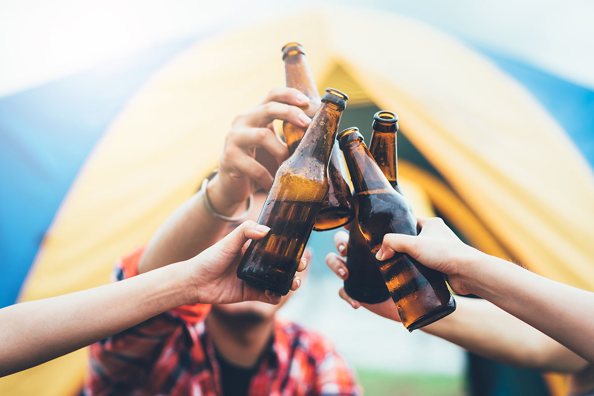 Friends clinking bottle of beer during travel camping trip outdoor