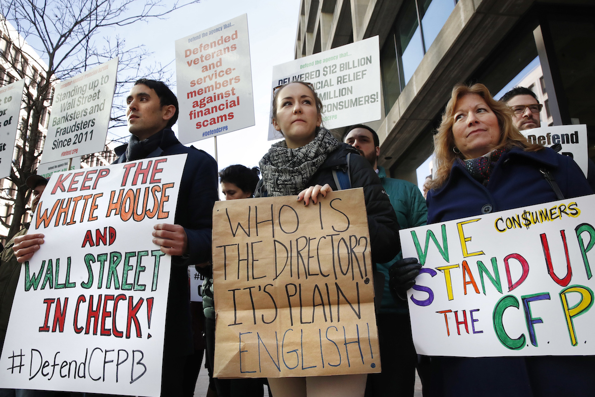 Mike Litt, left, Kaitlyn Vitez, and Ruth Susswein, gather with other members of consumer advocate groups to protest outside of the Consumer Financial Protection Bureau in Washington on Nov. 27, 2017, during a news conference with consumer groups that oppose Mick Mulvaney being named acting director for the bureau.