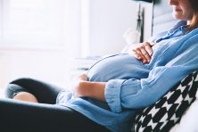 pregnant woman sitting on bed and holding belly in bedroom at home.