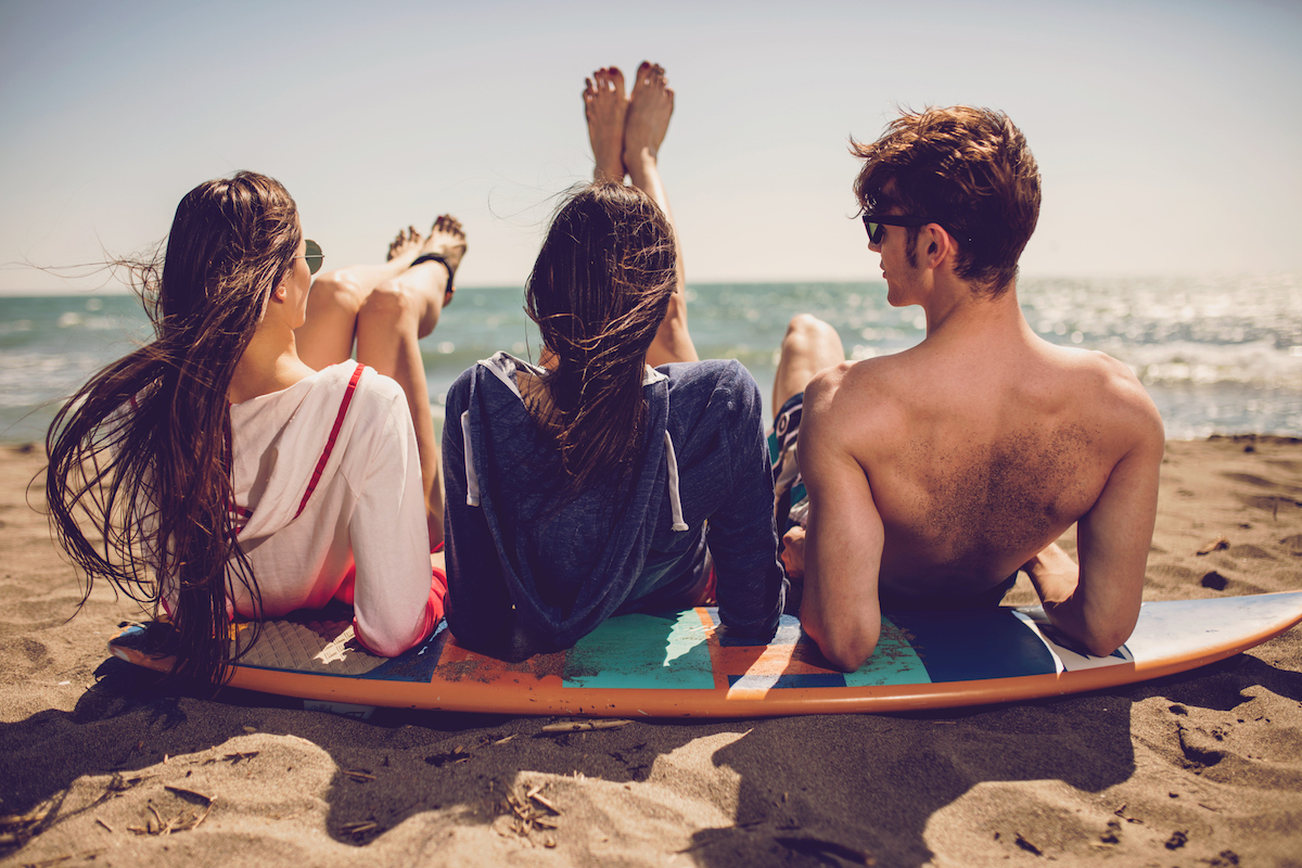 Group of smiling friends wearing swimwear and sunglasses with surfboards on beach. Summer concept, friends, friendship, summer fun, young people having fun