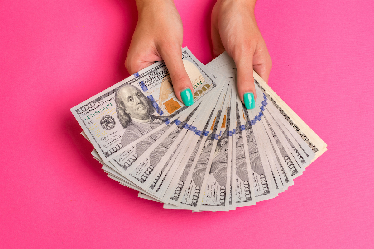 a womans hand holding money on a pink background