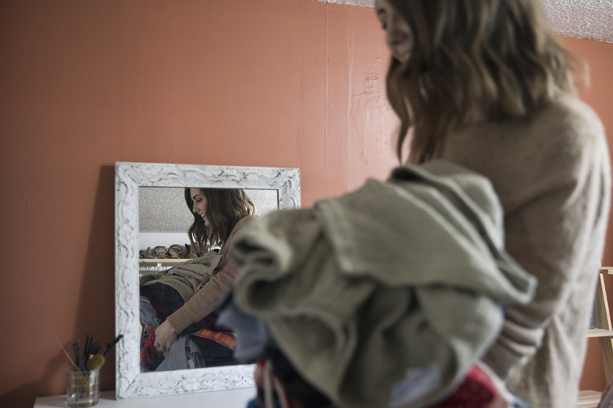 A woman carries piles of clothes to her bedroom to sort through.