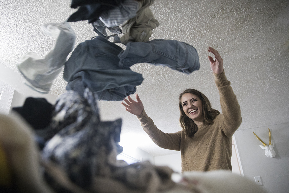 A woman throws a pile of clothes onto her bed.