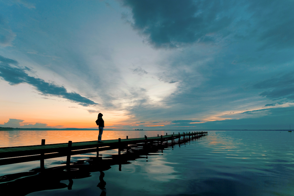 Silhouette of Woman on Lakeside Jetty with Cloudscape