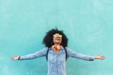 A woman looks happily at the sky against a turquoise wall.