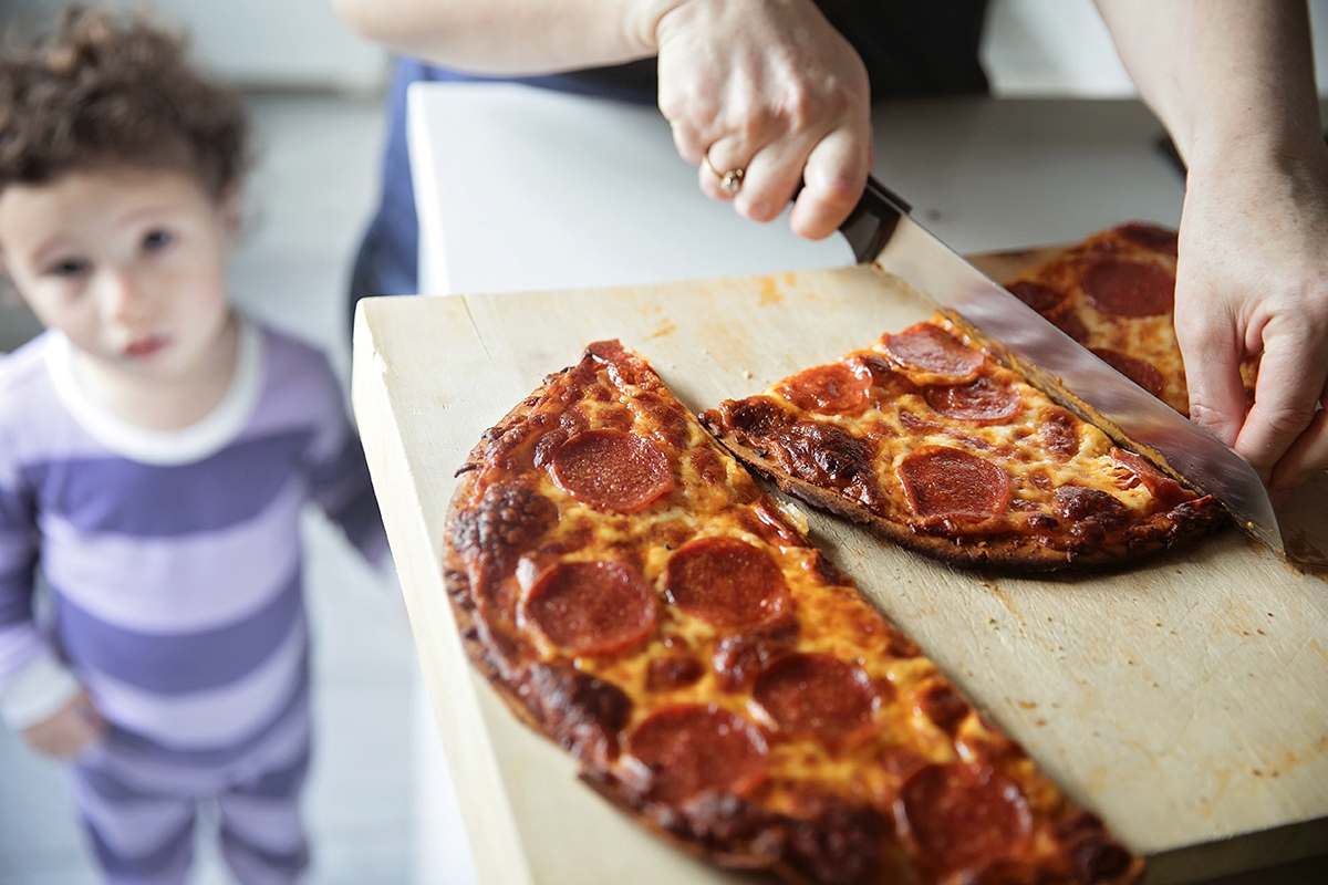 A woman cuts a baked pizza as her child looks on.