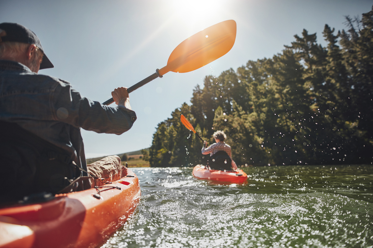 Outdoor shot of senior man canoeing in the lake with woman in background on a summer day