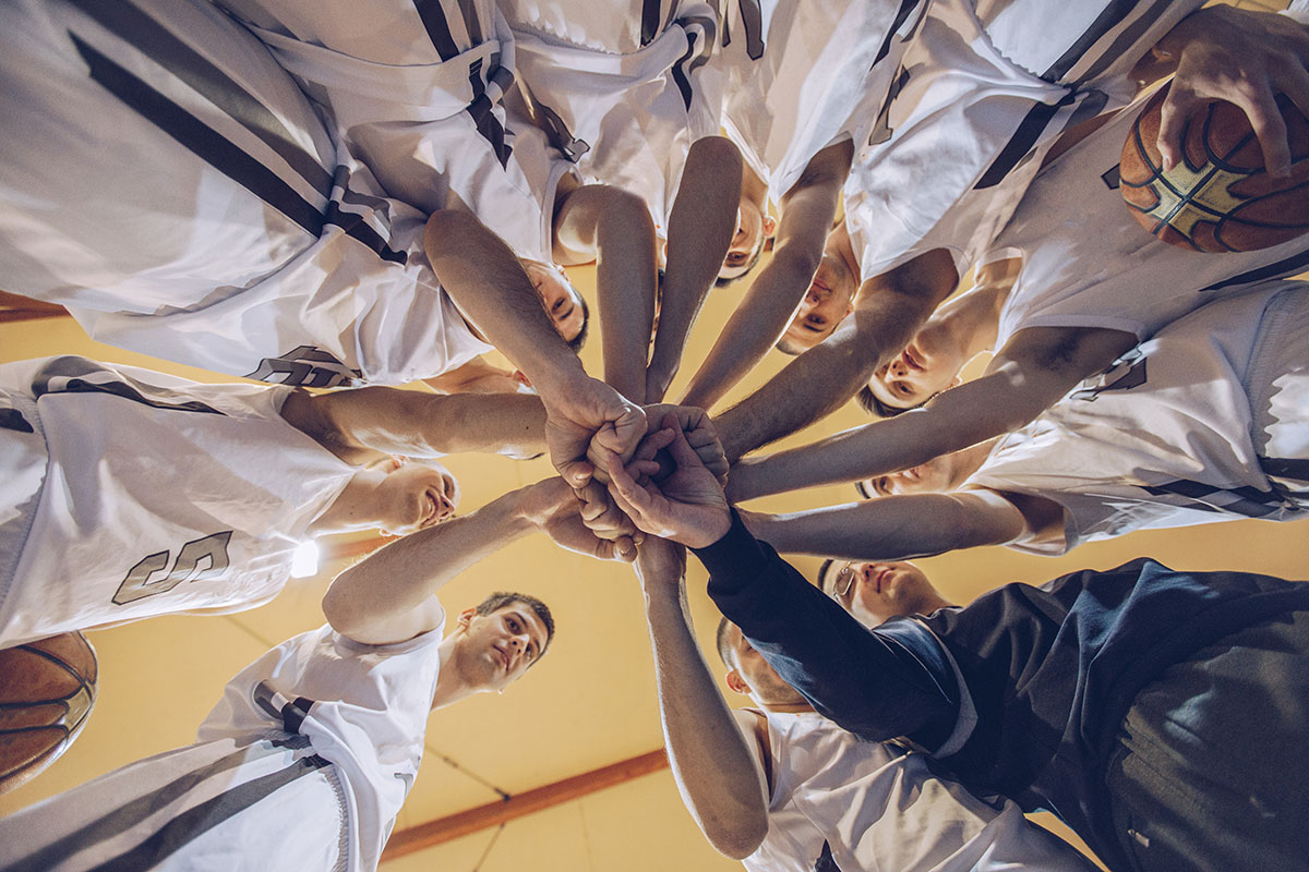 Group of men, basketball team and coach standing in circle, holding hands, low angle view.
