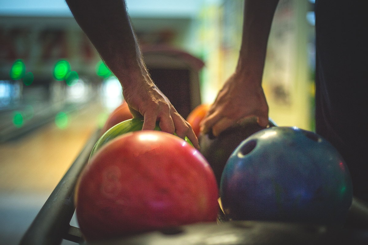 Colorful image of a few bowling balls in a row and two men are taking their balls to throw