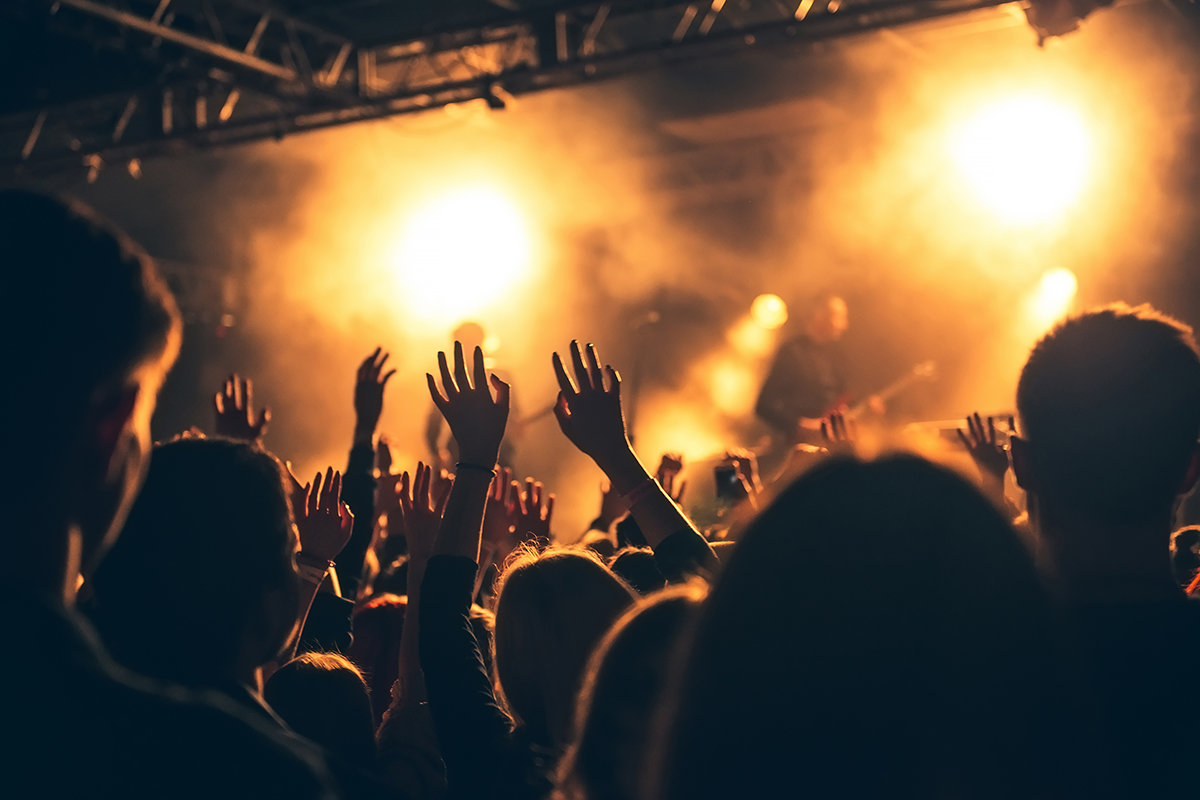 Silhouettes of people in a bright in the pop rock concert in front of the stage.