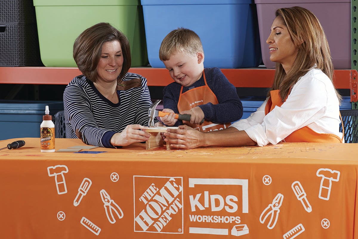 Two women help a child build a birdhouse at The Home Depot.