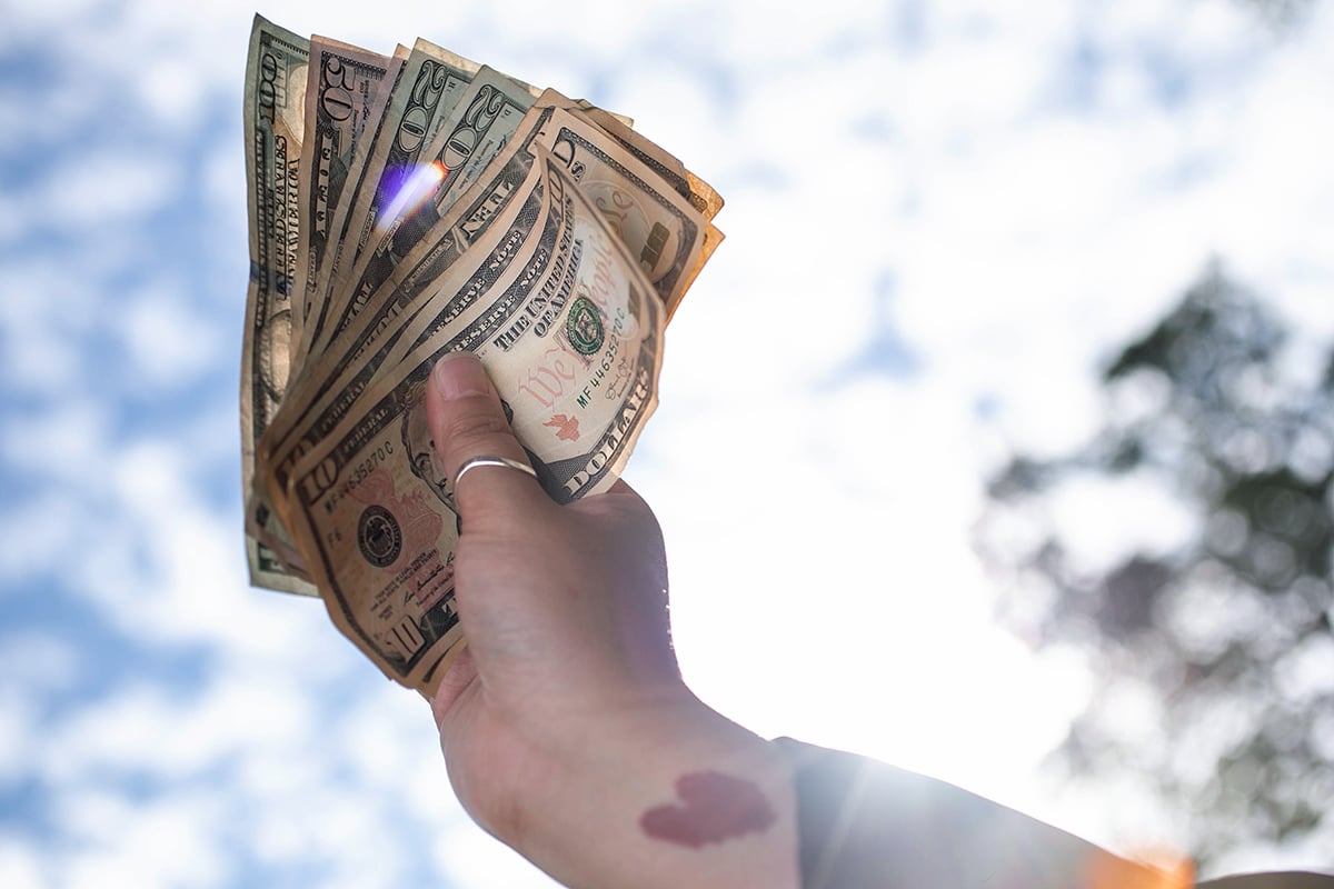 hand raised against the sky with dollar bills
