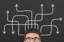 A man looks up to a bunch of squiggly lines lines on a chalkboard above his head.