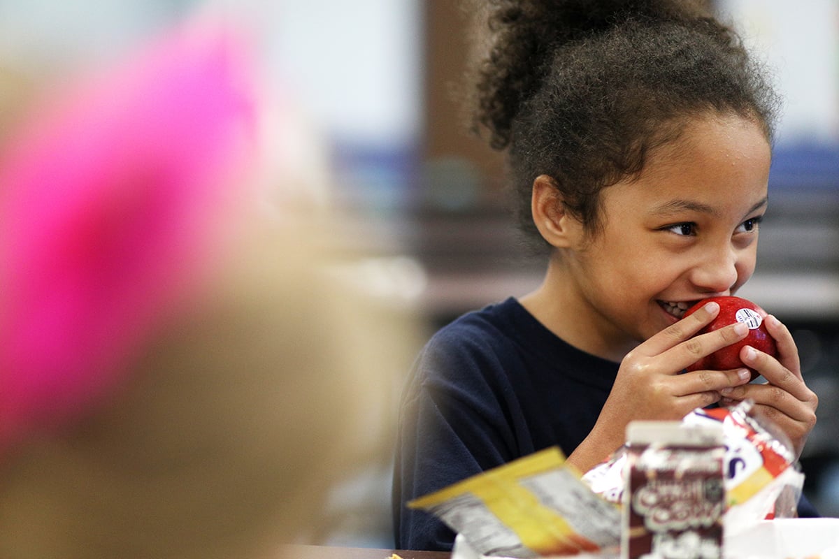 A girls eats an apple at lunchtime.