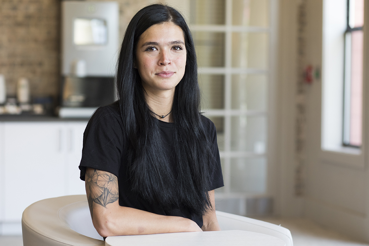 A woman with long dark hair and tattoos poses for a portrait.