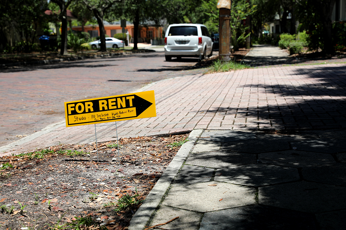 A for rent sign stands outside of a home for rent.
