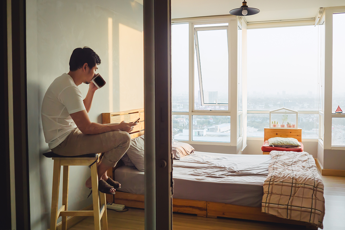 Lonely man chatting smartphone and drinking coffee in his room and watching sunset.