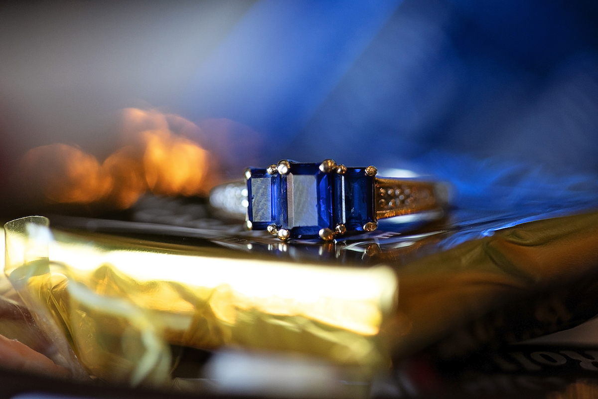 A three-stone imitation sapphire ring on a shiny surface.