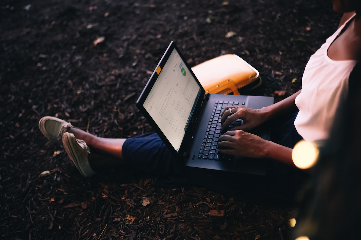 A laptop sits on the lap of a woman who is sitting on the floor.