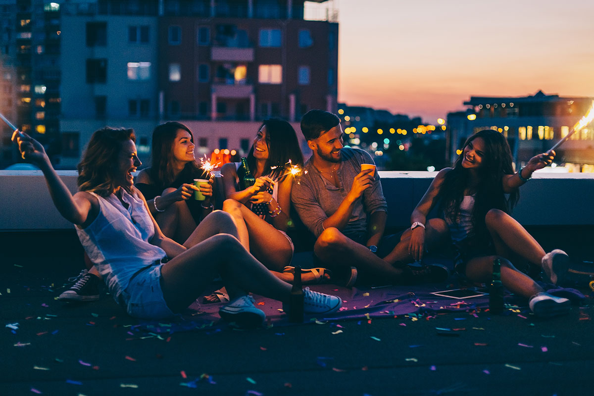 Happy friends partying on the rooftop with drinks and sparklers