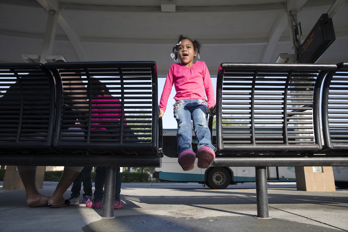 Nevaeh Gamble, 4, swings back and forth on the benches while waiting for the bus to arrive with her mother and sisters at Grand Central Station in St. Petersburg, Florida, on April 20, 2018.