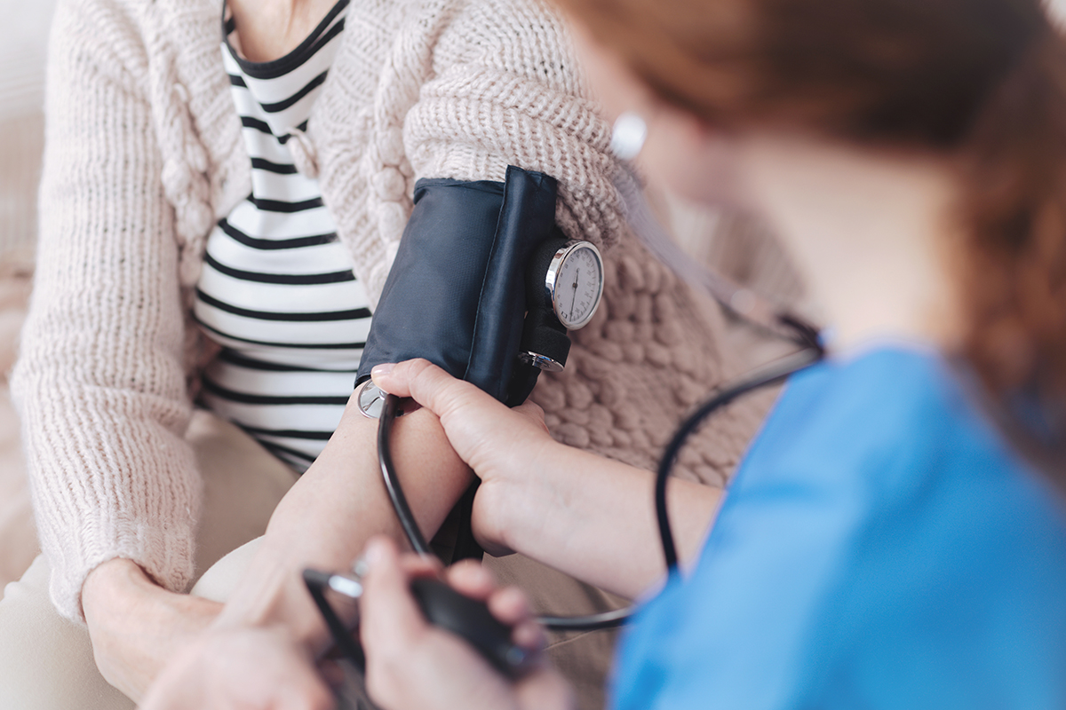 Close up view on a female nurse sitting in front of a senior patient while measuring her blood pressure during a regular visit.