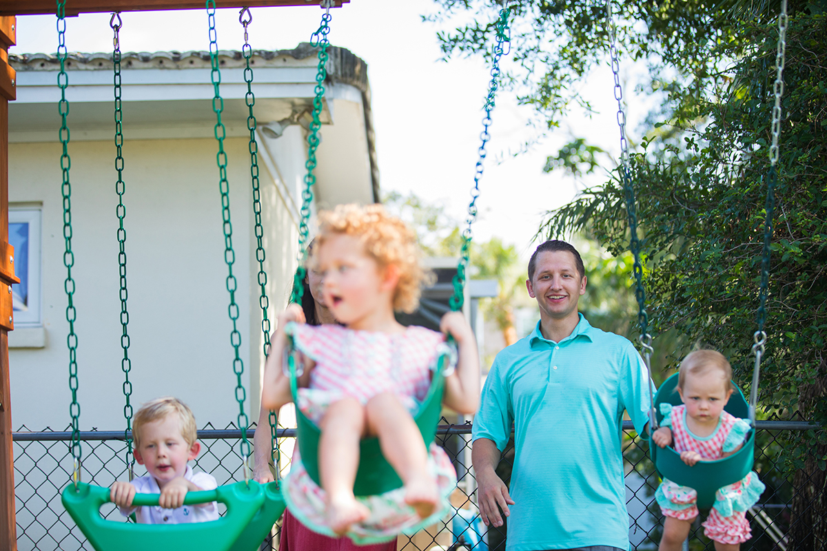 A dad pushes his children on the swing