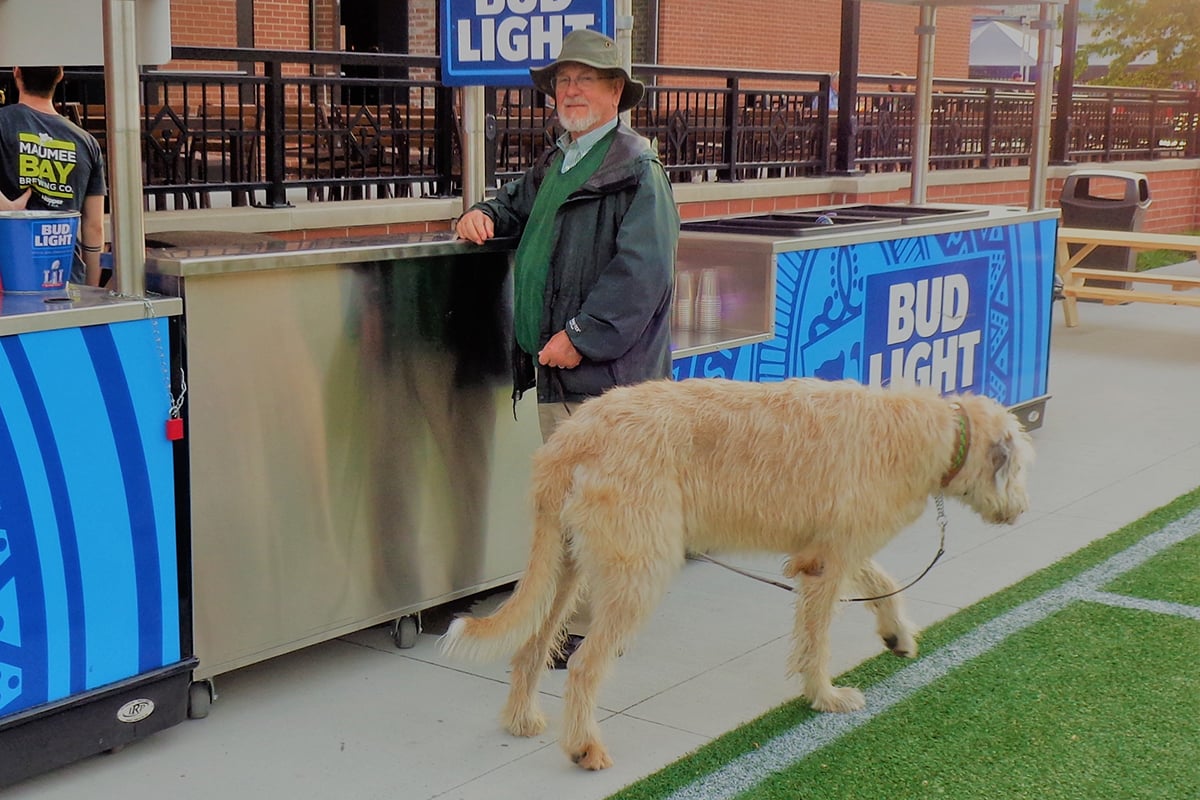 Bill Poznanski and his dog Hogan stand in front of a Budweiser booth