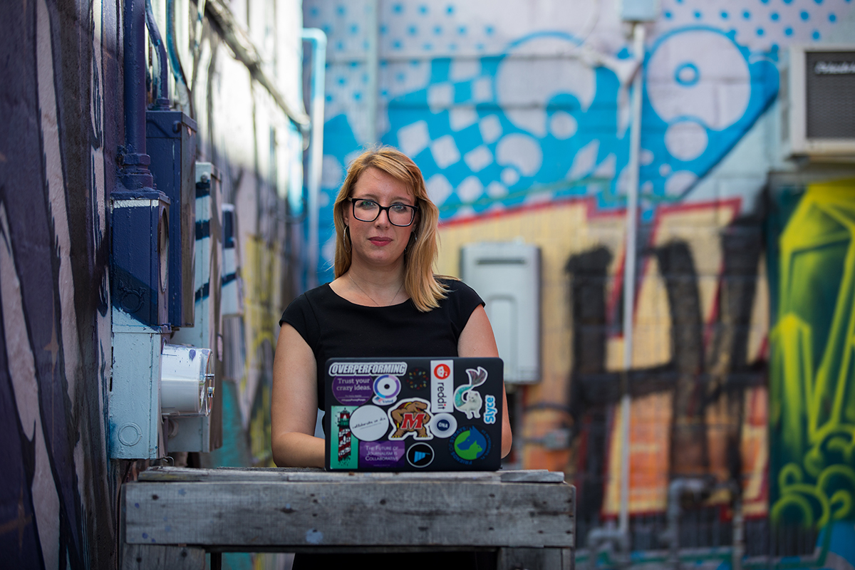 Lisa Rowan poses for a portrait in front of a mural with her laptop