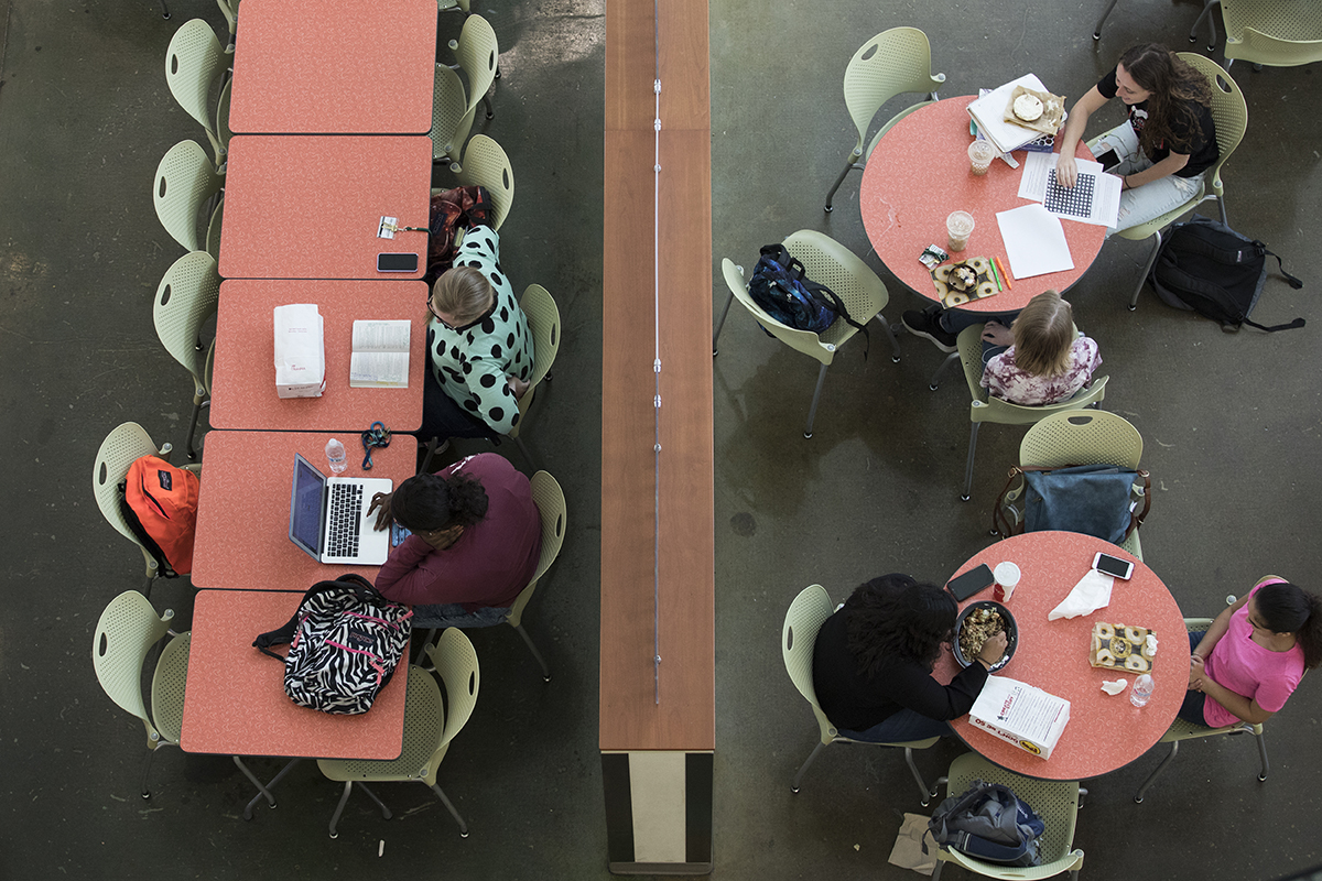 college students study and eat while sitting at tables on campus.