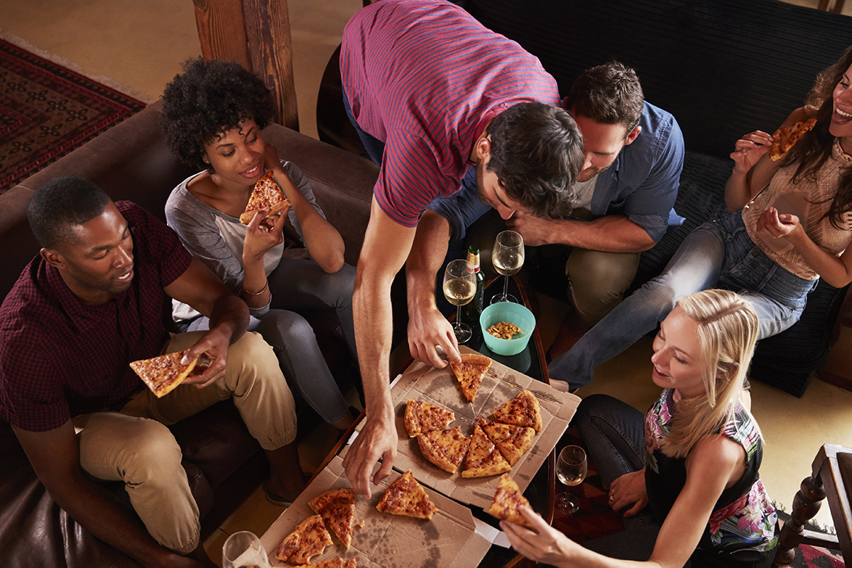 Young adults eating pizzas at a party at home